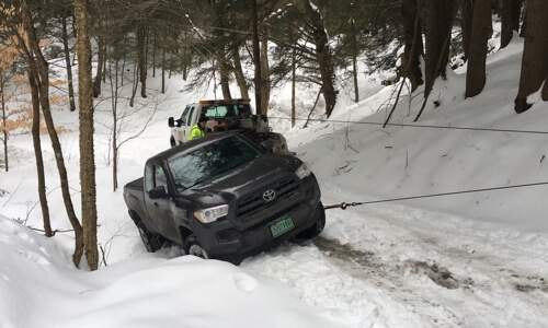 Holiday Pre-Trip Inspection, FanSection...Are They Worth It? with Girlington Garage in South Burlington, VT. image of toyota pickup with vermont plates being pulled out of snowy embankment