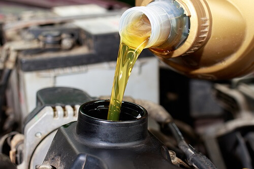 Critical Car Maintenance Tips | Girlington Garage in South Burlington, VT. Image of a car mechanic pouring engine oil on a car engine. Oil change is one of the critical vehicle maintenance.