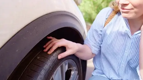 Here’s When to Repair or Replace Flat Tires | Girlington Garage in South Burlington, VT. Image of woman checking a punctured or flat tire of her car.