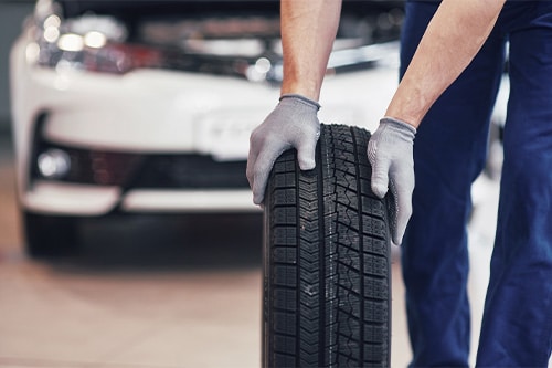 A tire mechanic holding a tire tire at the repair garage, changing winter and summer tires.